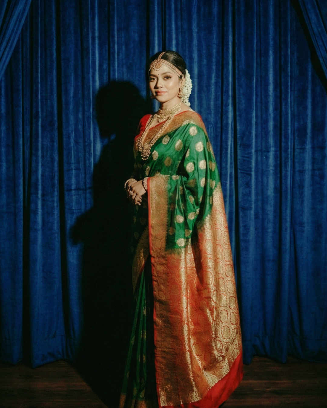 Woman in a traditional saree standing against a blue curtain